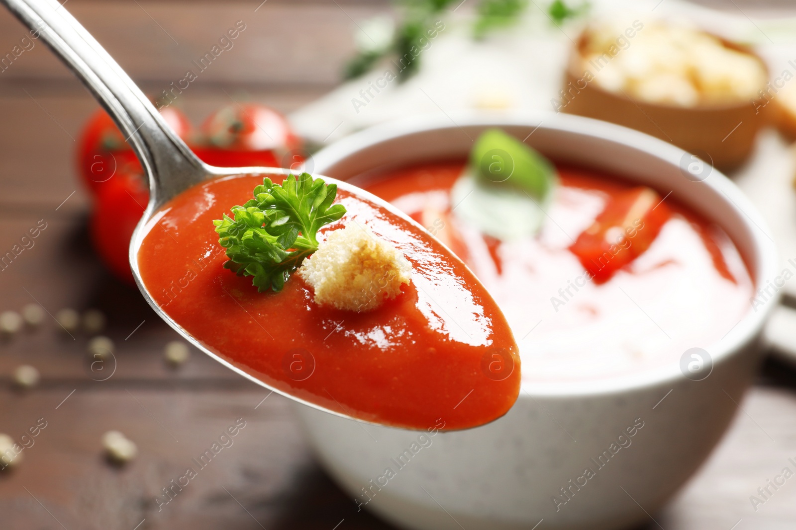 Photo of Spoon with fresh homemade tomato soup on blurred background, closeup. Space for text