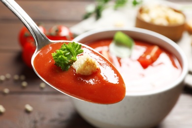 Spoon with fresh homemade tomato soup on blurred background, closeup. Space for text