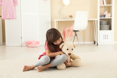 Cute little girl playing with teddy bear at home