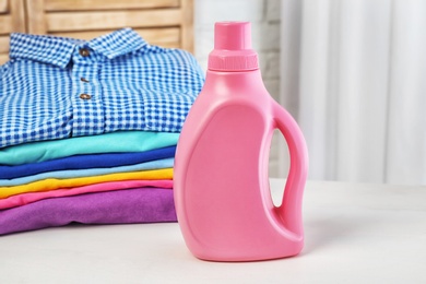 Photo of Stack of clean clothes and bottle with detergent on table