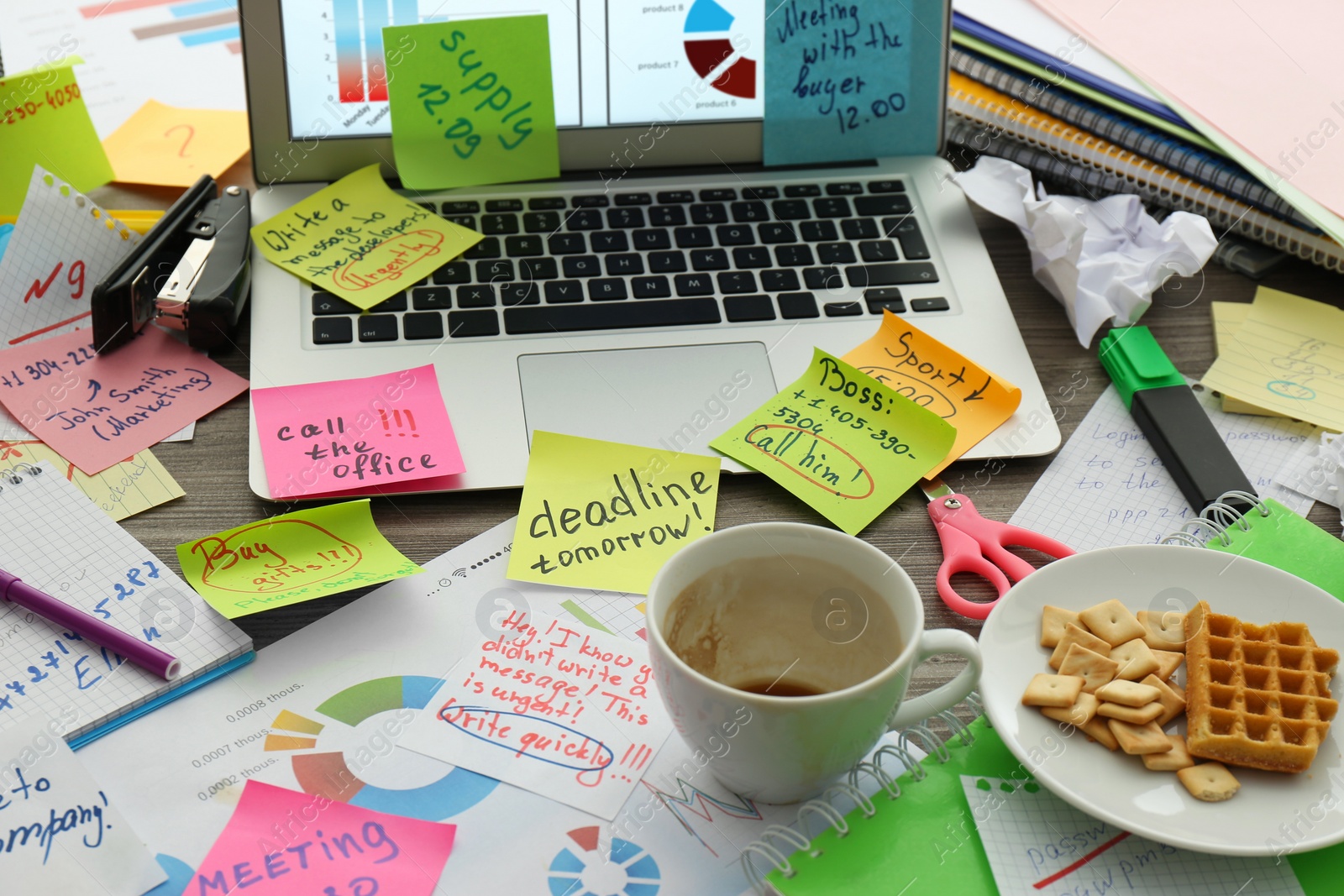 Photo of Laptop, notes and office stationery in mess on desk. Overwhelmed with work