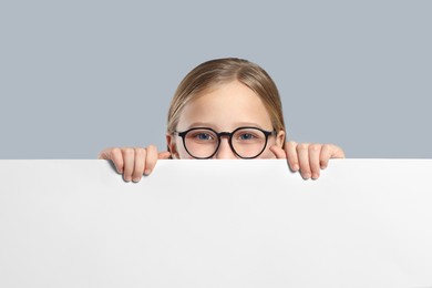 Photo of Cute girl looking out of placard on light grey background. Space for text