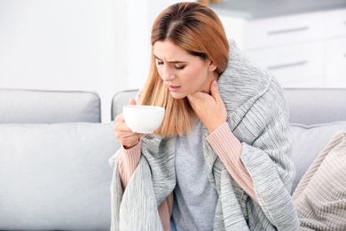 Photo of Woman with cup of tea for cough on sofa at home