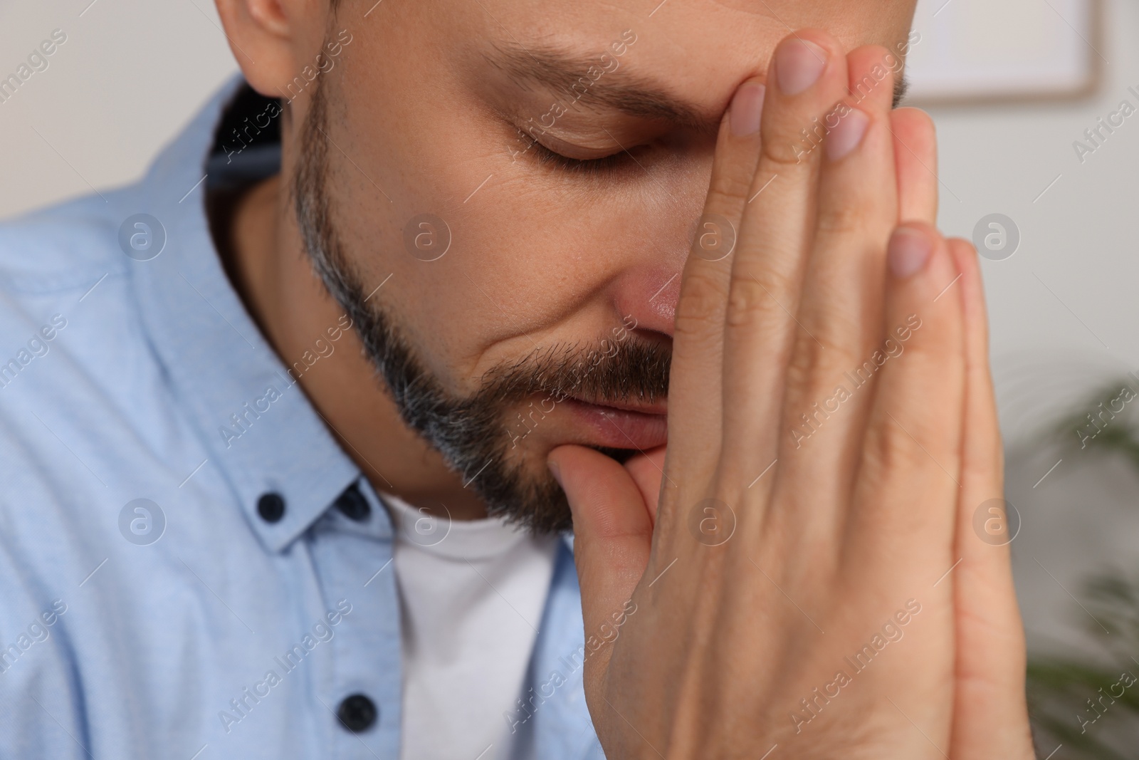 Photo of Man with clasped hands praying indoors, closeup