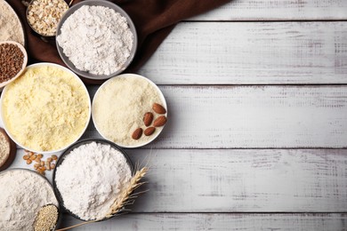 Bowls with different types of flour and ingredients on white wooden table, flat lay. Space for text