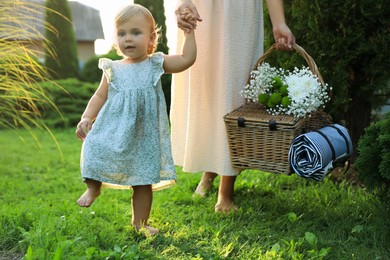 Photo of Adorable baby girl and her mother with picnic basket in garden on sunny day