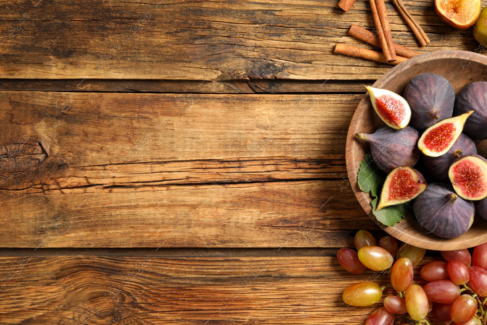 Photo of Tasty fresh figs, cinnamon and grapes on wooden table, flat lay. Space for text
