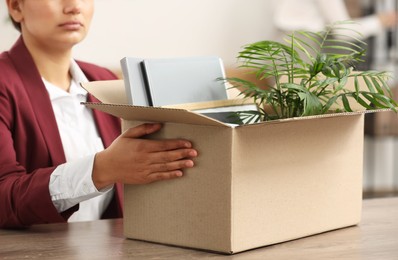 Photo of Unemployment problem. Woman with box of personal belongings at table in office, closeup