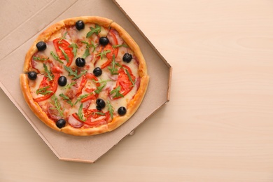 Cardboard box with tasty pizza on wooden background, top view with space for text