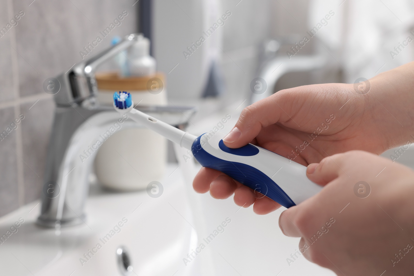 Photo of Woman holding electric toothbrush near sink in bathroom, closeup