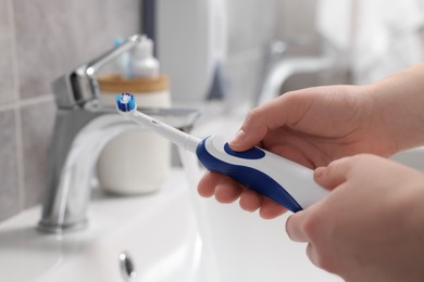 Photo of Woman holding electric toothbrush near sink in bathroom, closeup