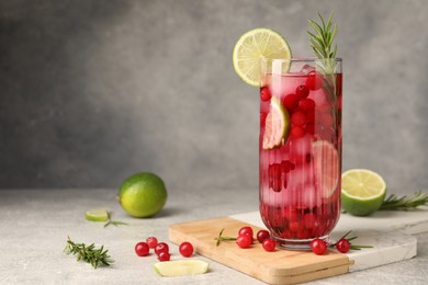 Photo of Tasty cranberry cocktail with rosemary and lime in glass on gray textured table, space for text