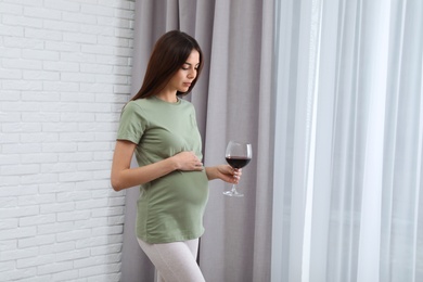 Photo of Future mother with glass of wine indoors, space for text. Alcohol abuse during pregnancy