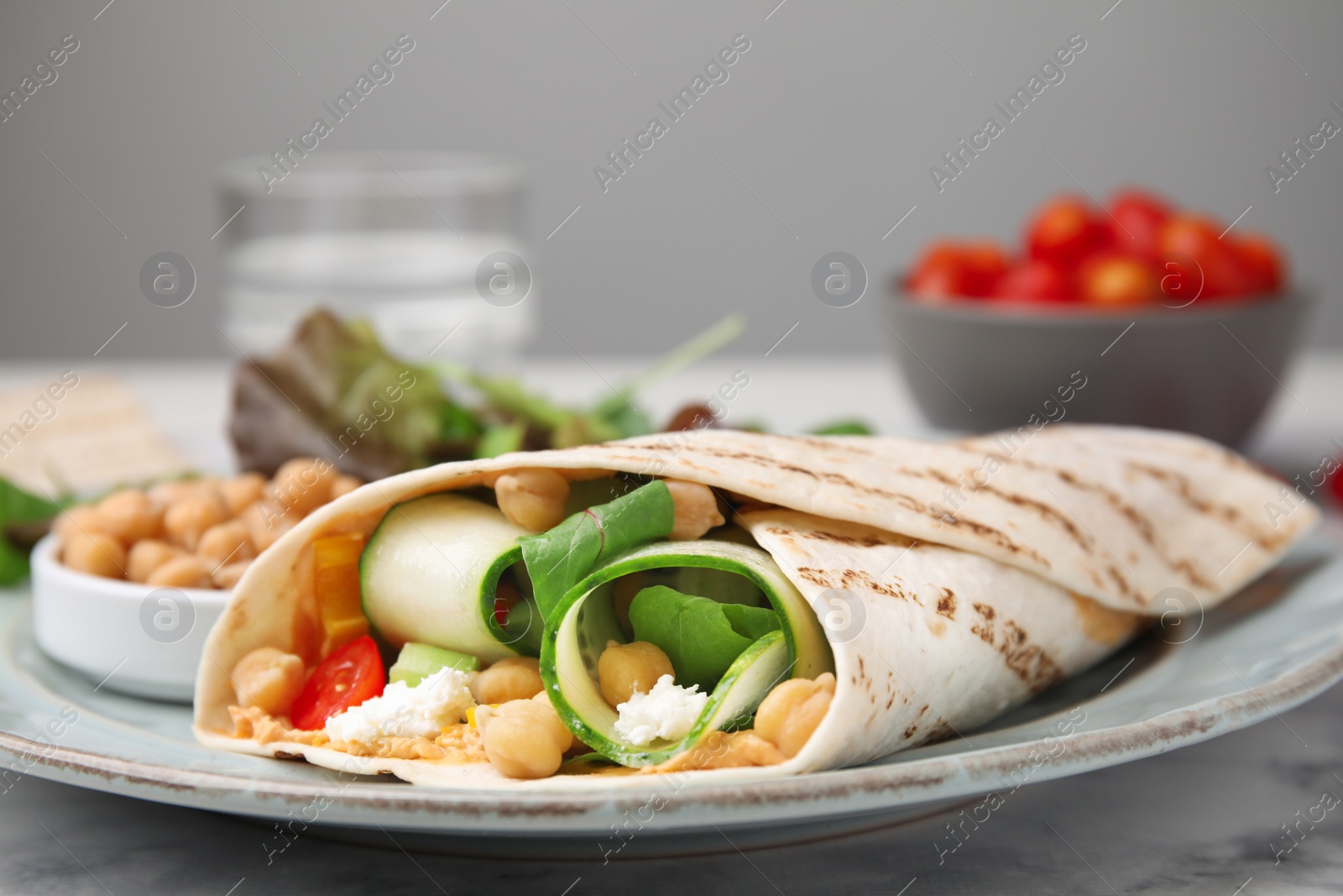 Photo of Delicious hummus wrap with vegetables on table, closeup. Space for text