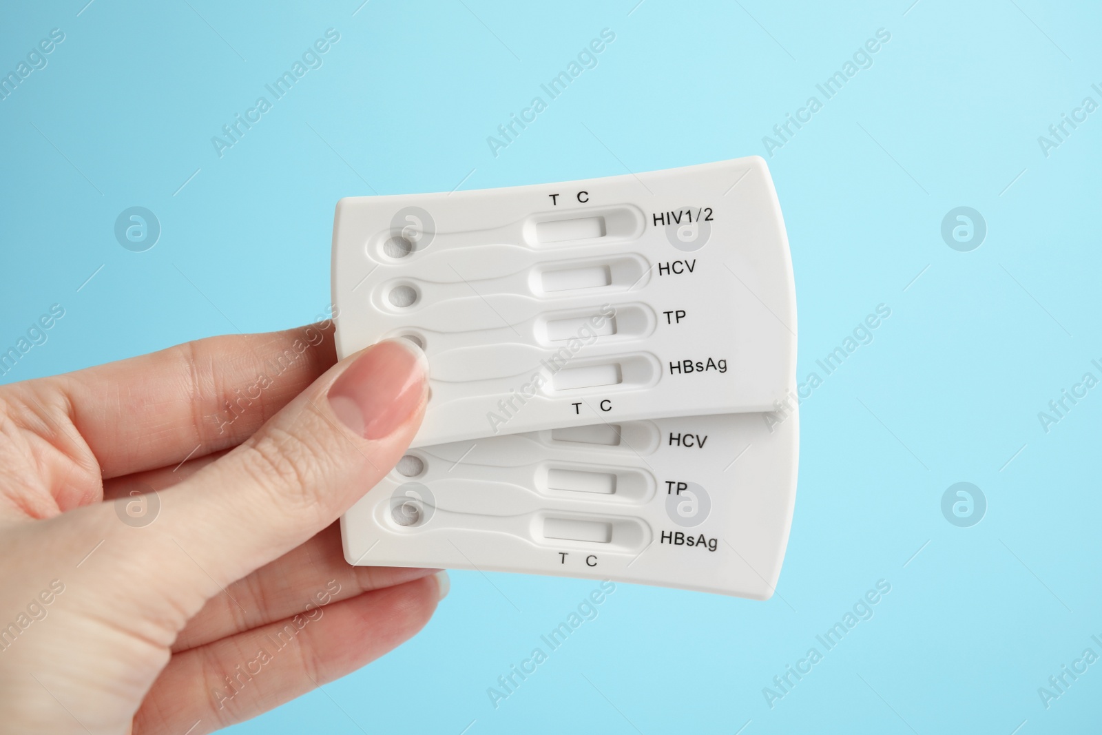 Photo of Woman holding two disposable express tests for hepatitis on light blue background, closeup