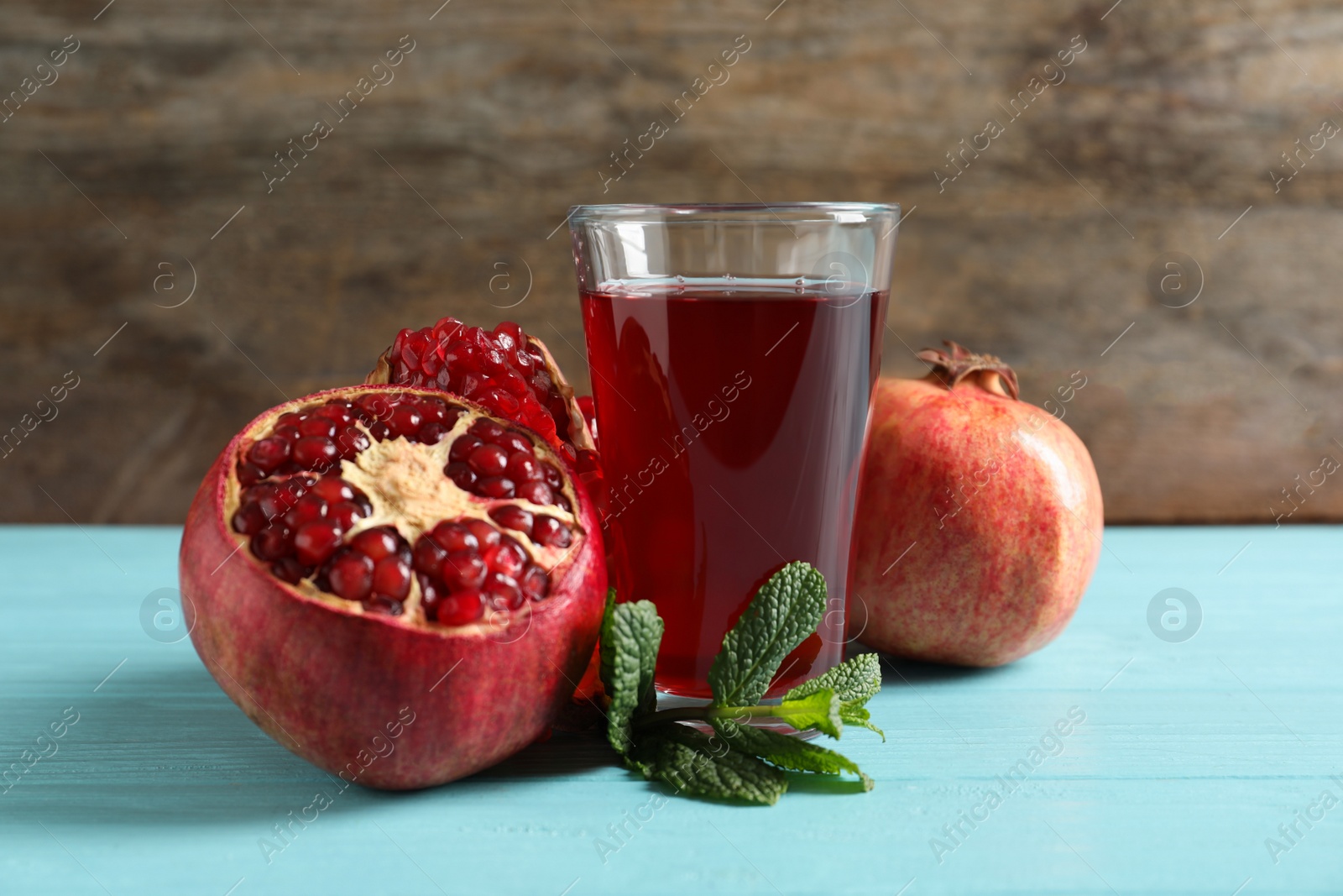 Photo of Glass of pomegranate juice and fresh fruits on table against wooden background