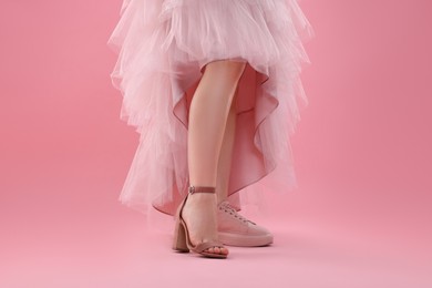 Photo of Woman wearing high heeled shoe and sneaker on pink background, closeup. Glamour vs comfort concept