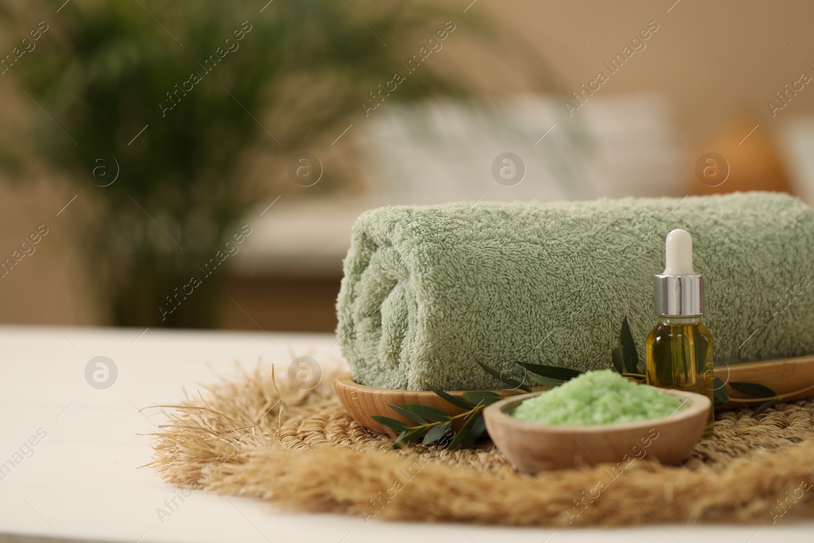 Photo of Spa composition. Rolled towel, cosmetic product, sea salt and twig on table indoors. Space for text