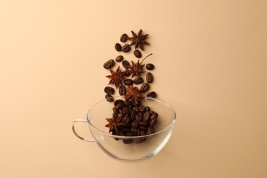Photo of Coffee beans and anise stars falling into glass cup on beige background, flat lay