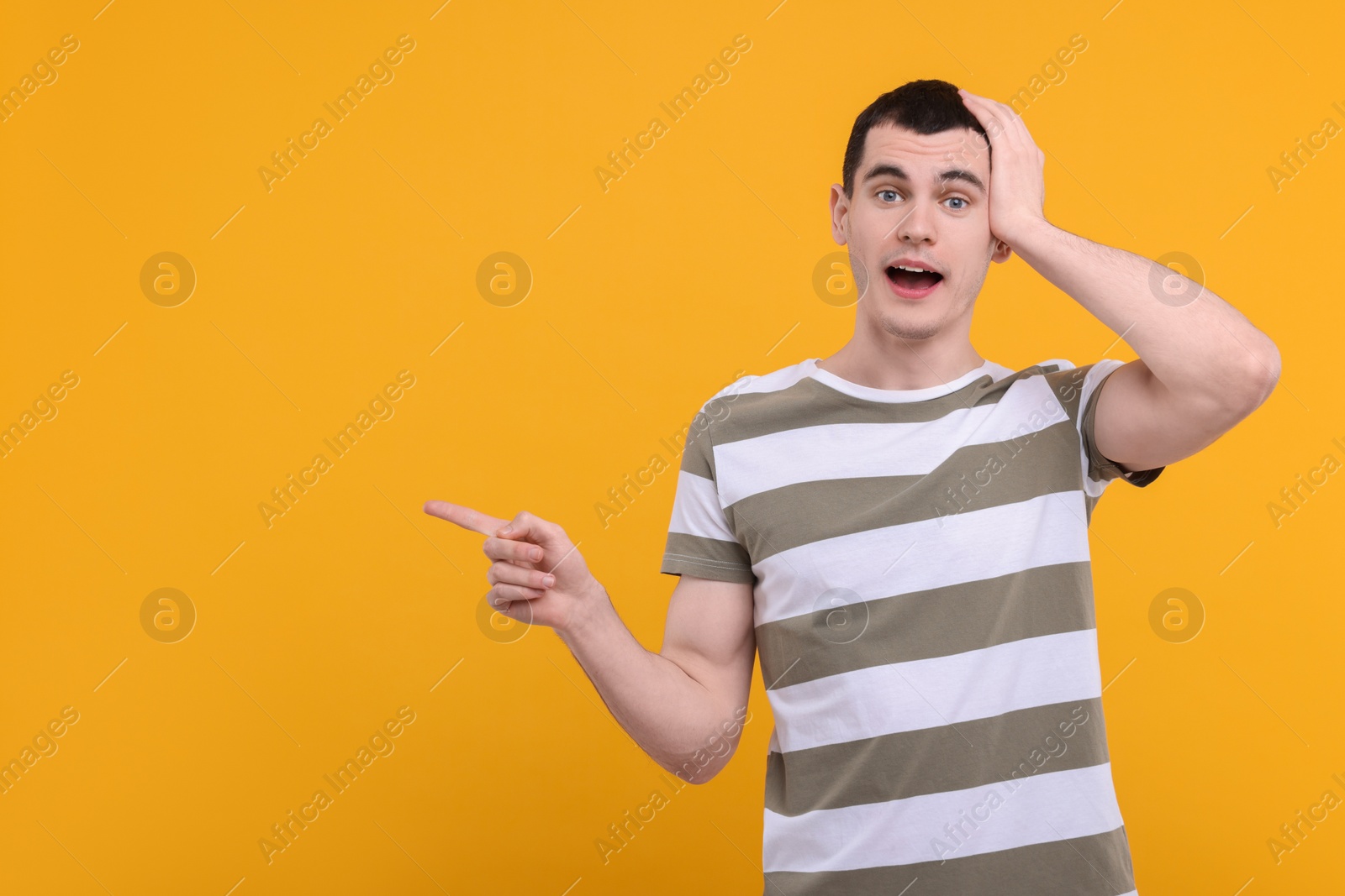 Photo of Surprised man pointing at something on orange background, space for text