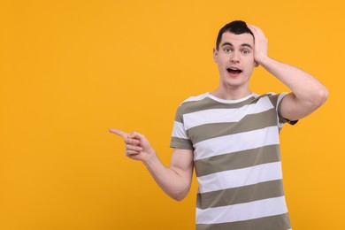 Surprised man pointing at something on orange background, space for text