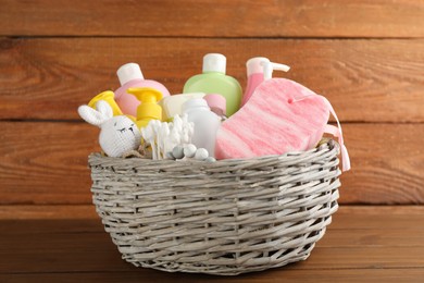 Photo of Wicker basket full of different baby cosmetic products, accessories and toys on wooden table