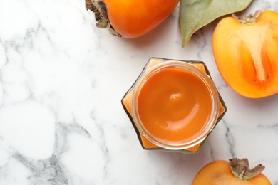 Photo of Delicious persimmon jam and fresh fruits on white marble table, flat lay. Space for text