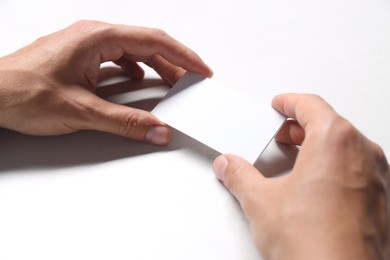 Photo of Man holding blank cards at white table, closeup. Mockup for design