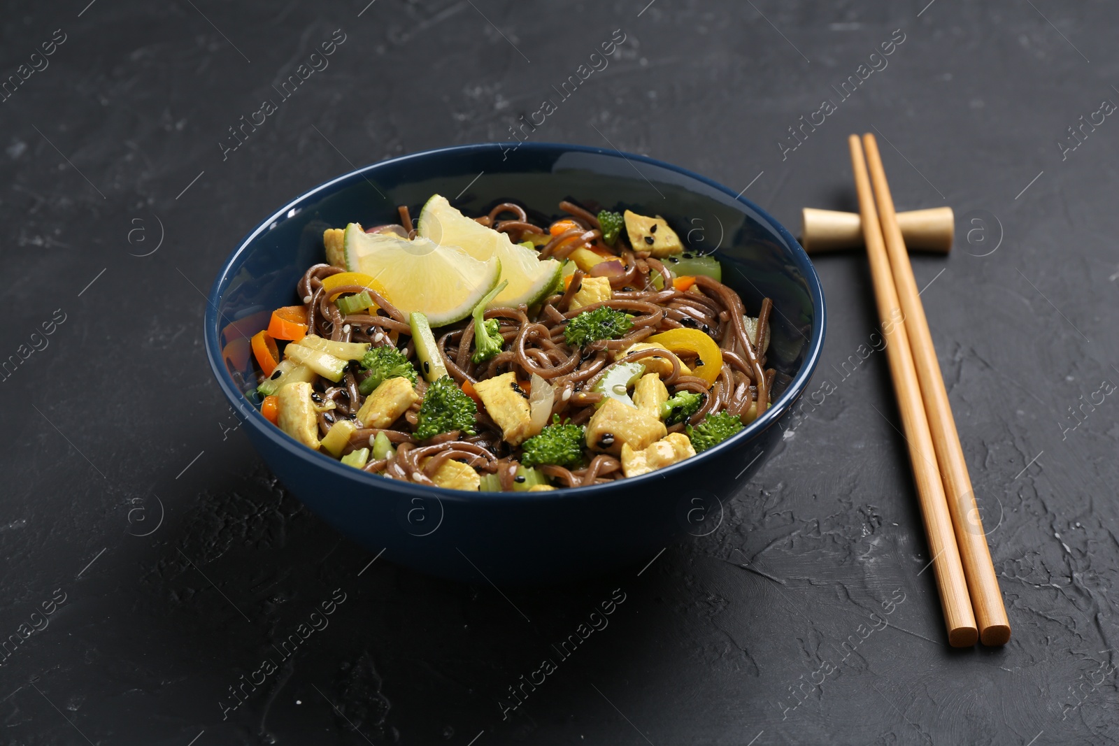 Photo of Stir-fry. Delicious cooked noodles with chicken and vegetables in bowl served on gray textured table