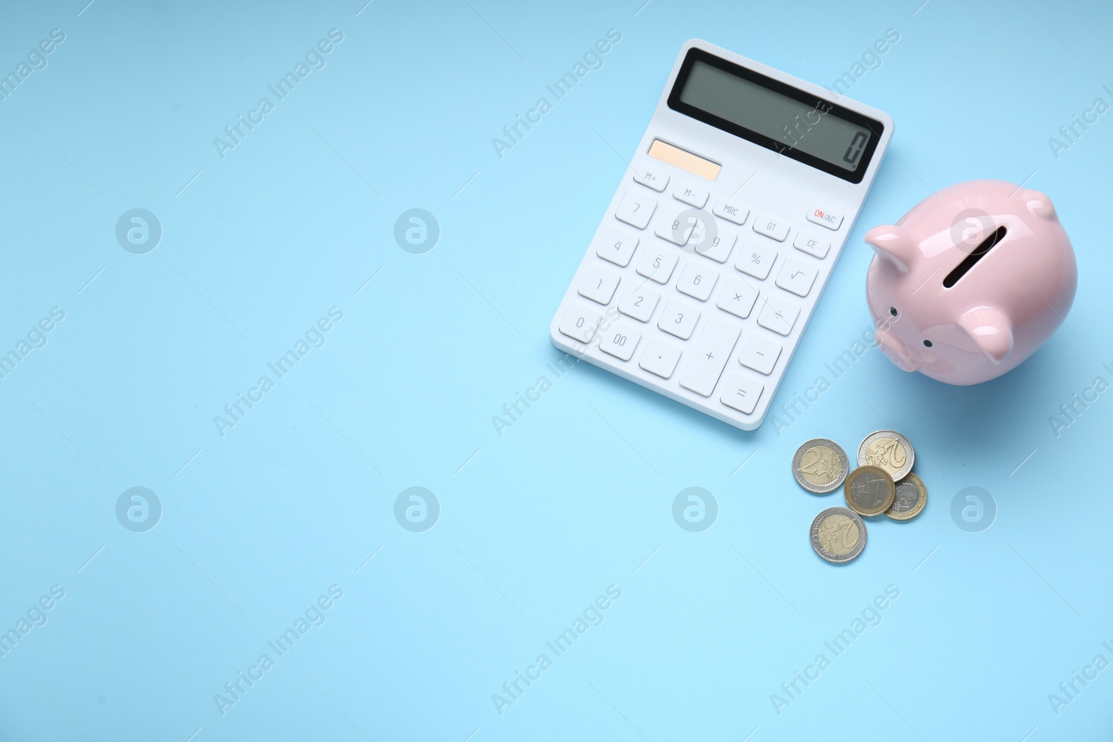 Photo of Piggy bank, coins and calculator on light blue background, flat lay. Space for text