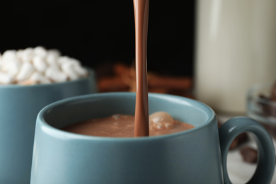 Pouring hot cocoa drink into cup on black background, closeup