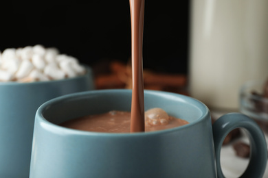 Photo of Pouring hot cocoa drink into cup on black background, closeup