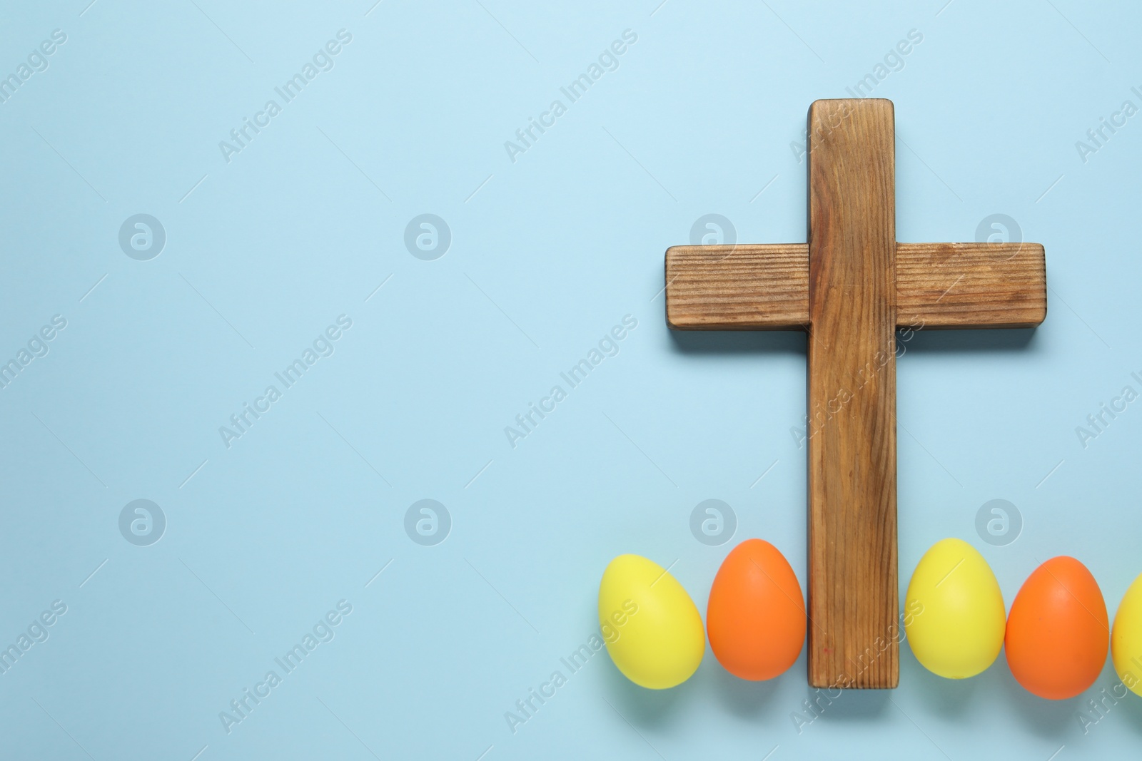 Photo of Wooden cross and painted Easter eggs on light blue background, flat lay. Space for text