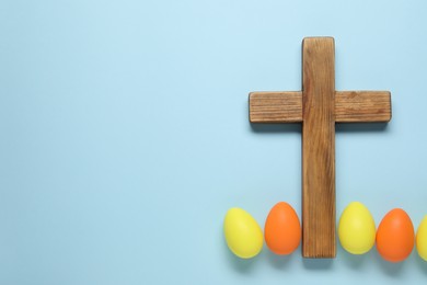 Photo of Wooden cross and painted Easter eggs on light blue background, flat lay. Space for text