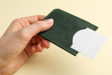 Woman holding business card holder with blank cards on light yellow background, closeup