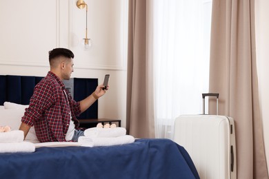 Photo of Handsome man using smartphone on bed in hotel room