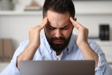 Photo of Man suffering from headache at workplace in office
