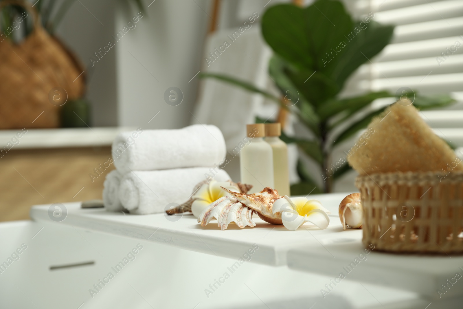 Photo of Bath tray with spa products, towels and shells on tub in bathroom