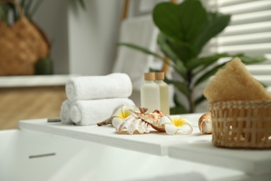 Photo of Bath tray with spa products, towels and shells on tub in bathroom
