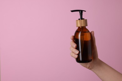 Woman holding bottle of cosmetic product on pink background, closeup. Space for text