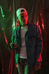 Photo of Young man with baseball bat on dark background in neon lights