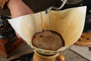 Photo of Woman pouring hot water into glass chemex coffeemaker with paper filter at table, closeup