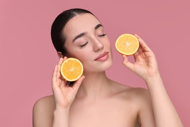 Photo of Beautiful young woman with pieces of orange on pink background