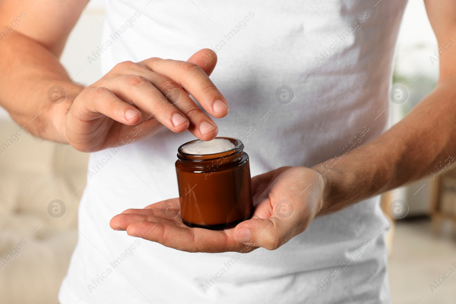 Photo of Man holding jar of hand cream indoors, closeup