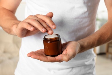 Man holding jar of hand cream indoors, closeup