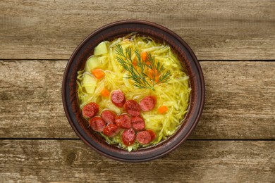 Photo of Bowl of delicious sauerkraut soup with smoked sausages and dill on old wooden table, top view