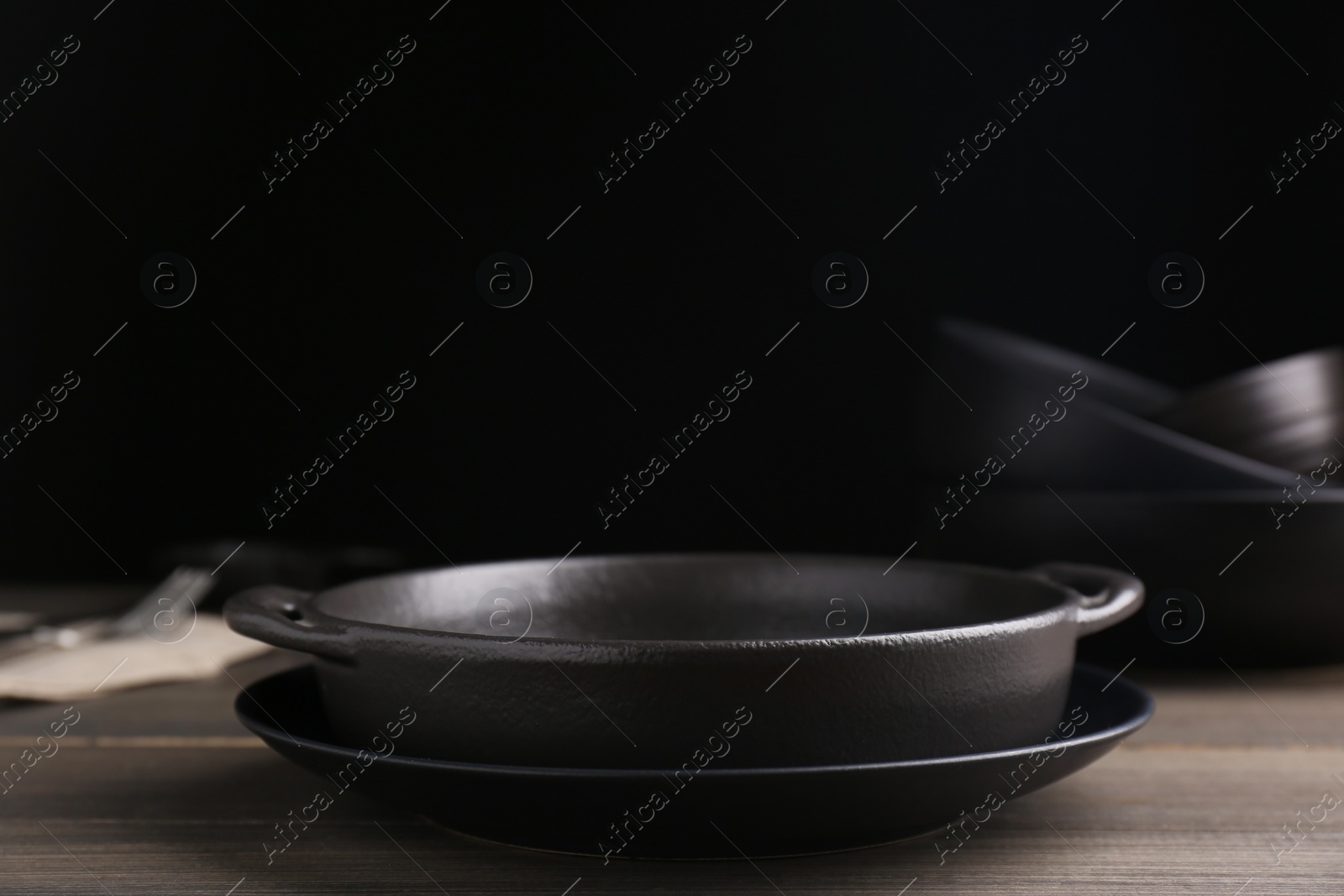 Photo of Black serving pan and plate on wooden table. Space for text