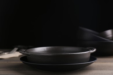 Black serving pan and plate on wooden table. Space for text