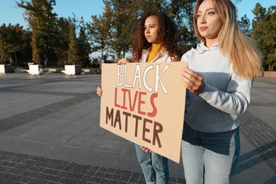 Women holding sign with phrase Black Lives Matter outdoors, space for text. Racism concept