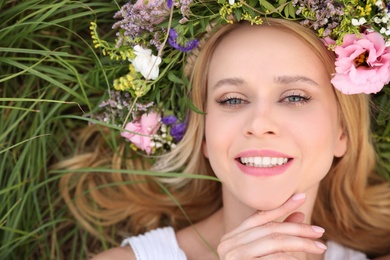 Photo of Young woman wearing wreath made of beautiful flowers on green grass, top view
